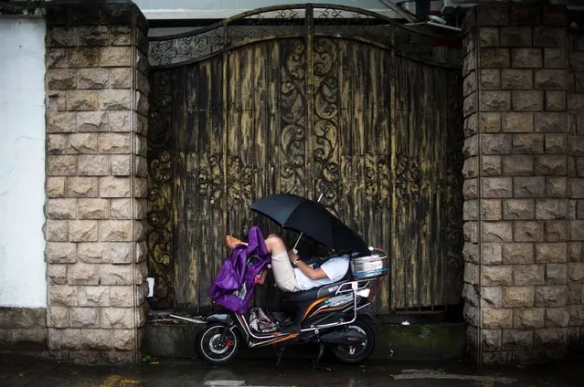 A man uses an umbrella to protect himself against the rain while having a nap on his scooter in Shanghai on July 14, 2016. (Photo by Johannes Eisele/AFP Photo)