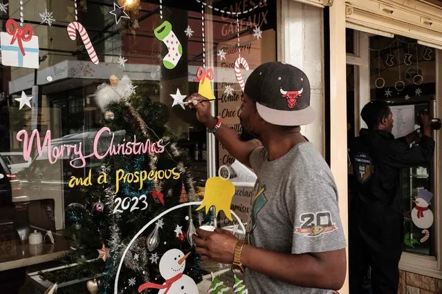 A Kenyan artist paints Christmas decorations on windows at a cafe in Nairobi on December 11, 2022. (Photo by Yasuyoshi Chiba/AFP Photo)