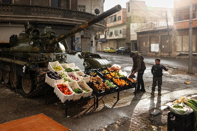 A Syrian man sells vegetables in front of a damaged tank in Homs, on December 20, 2024. Islamist-led rebels took Damascus in a lightning offensive on December 8, ousting president Bashar al-Assad and ending five decades of Baath rule in Syria. (Photo by Sameer Al-Doumy/AFP Photo)