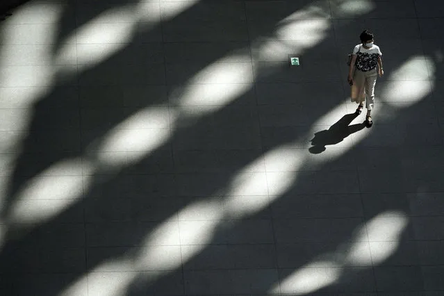 A woman wearing a protective mask to help curb the spread of the coronavirus walks in the shade of a building Friday, September 4, 2020, in Tokyo. (Photo by ugene Hoshiko/AP Photo)