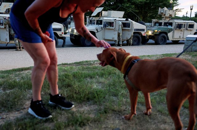 A woman pets a dog as people enjoy a night out at the National Mall, near where National Guard Humvees are parked by the Washington Monument, on August 12, 2025. (Photo by Jonathan Ernst/Reuters)