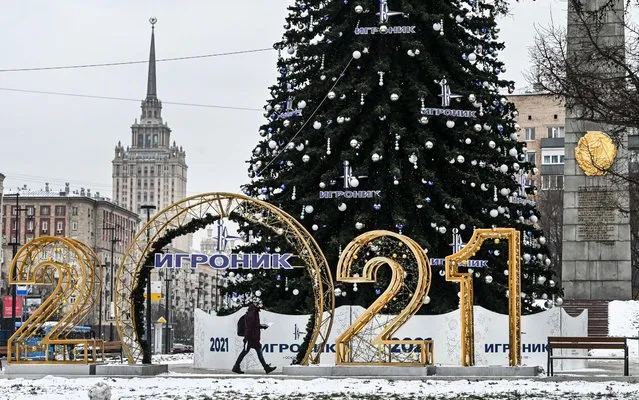 A man walks next to a Christmas decoration in front of a five-star Radisson Collection Hotel (L) on the bank of the Moskva River, formerly known as Hotel Ukraine, one of the city's seven 1950's Stalin skyscrapers, in central Moscow on December 24, 2020, amid the Covid-19 pandemic crisis caused by the novel coronavirus. Russia hits two new records confirming 29,935 new Covid-19 daily cases including 8,203 in Moscow. (Photo by Alexander Nemenov/AFP Photo)