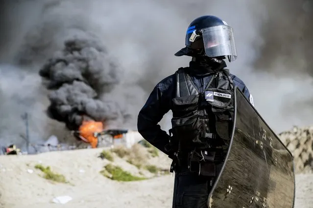 A French riot police officer forbids migrants and journalist to access the makeshift camp “The Jungle” after several fires set the whole area on fire during its evacuation in Calais, France, 26 October 2016. The incident has pushed the authorities to speed up the evacuation process that shall be over tonight. The camp gathering more than 7,000 migrants started being dismantled on Monday, a process that shall take a week according tho the French authorities. (Photo by Etienne Laurent/EPA)