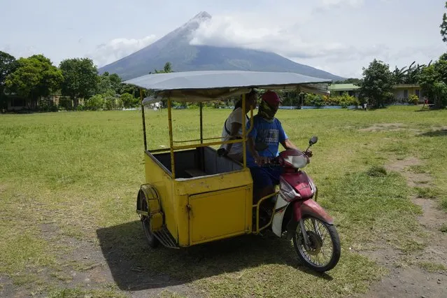 Mayon Volcano is seen as a tricycle passes by an evacuation center in Santo Domingo town, Albay province, northeastern Philippines, Tuesday, June 13, 2023. (Photo by Aaron Favila/AP Photo)