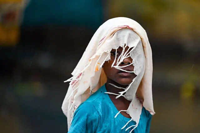 A boy covers himself with a cloth while walking along a street, as it rains in Chennai on June 19, 2023. (Photo by R.Satish Babu/AFP Photo)