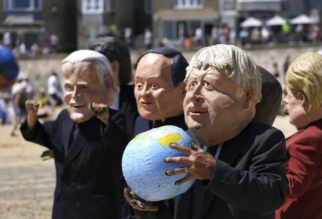 Protestors wearing giant heads portraying G7 leaders participate in a demonstration on a beach outside the G7 meeting in St. Ives, Cornwall, England, Sunday, June 13, 2021. (Photo by Jon Super/AP Photo)