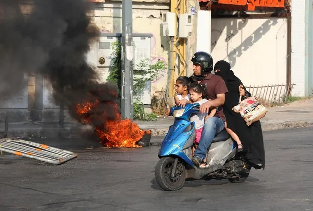 A man rides on a motorbike past a burning tyre, during a demonstration by relatives of some of the victims of last year's Beirut port blast, near the Justice Palace in Beirut, Lebanon on July 14, 2021. (Photo by Mohamed Azakir/Reuters)