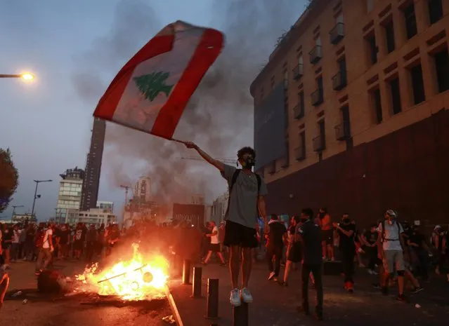 A demonstrator holds the Lebanese flag during a protest near parliament, as Lebanon marks the one-year anniversary of the explosion in Beirut, Lebanon on August 4, 2021. United in grief and anger, families of the victims and other Lebanese came out into the streets of Beirut on Wednesday to demand accountability as banks, businesses and government offices shuttered to mark one year since the horrific explosion. (Photo by Aziz Taher/Reuters)