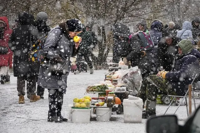 A woman chooses apples from a street vendor in snowfall in St. Petersburg, Russia, Tuesday, November 21, 2023. (Photo by Dmitri Lovetsky/AP Photo)