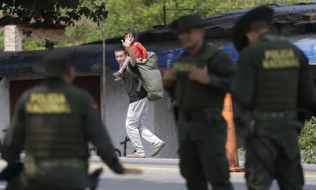 A Venezuelan migrant waves at Colombian police as he walks past in Los Patios, near Cucuta, Colombia, Thursday, February 7, 2019. Humanitarian assistance from the U.S. for Venezuelan over objections from President Nicolas Maduro, has arrived in Cucuta. (Photo by Fernando Vergara/AP Photo)
