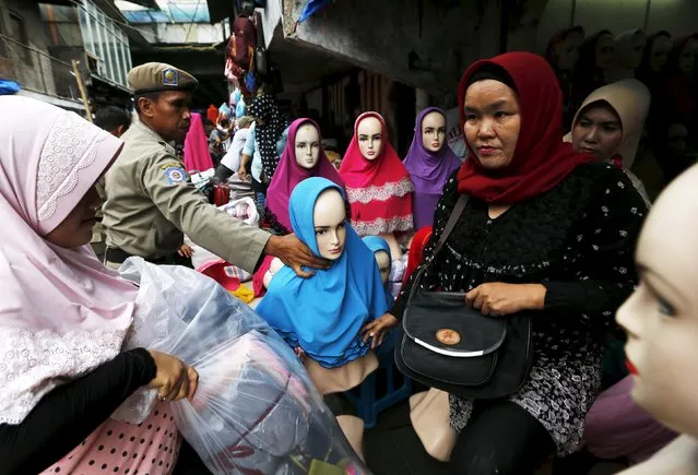 A hijab vendor (L) gathers her belongings as a Civil Service policeman (2nd L) moves her manequin near a customer (R) during a sweep operation on illegal steet vendors, causing traffic congestion at Tanah Abang market in Jakarta, April 7, 2015. (Photo by Reuters/Beawiharta)