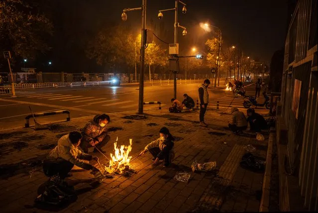 A family burns fake paper money and other items in a ritual in memory of recently deceased relatives on a street on November 5, 2021 in Beijing, China. Burning paper money, known as joss paper, is a traditional Chinese-Taoist practice that people believe will send money and goods to relatives in the afterlife. Due to the closure of religious sites due to COVID-19 control measures, some people who would usually take part in the ritual at a local temple performed it in the street. (Photo by Kevin Frayer/Getty Images)