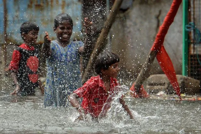 Children play at a waterlogged street near a residential area after heavy monsoon rainfall in Chennai on November 12, 2021. (Photo by Arun Sankar/AFP Photo)