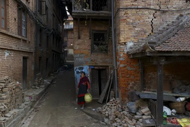 A woman walks out holding a bucket from her damaged house to fetch water, a month after the April 25 earthquake in Kathmandu, Nepal May 25, 2015. (Photo by Navesh Chitrakar/Reuters)