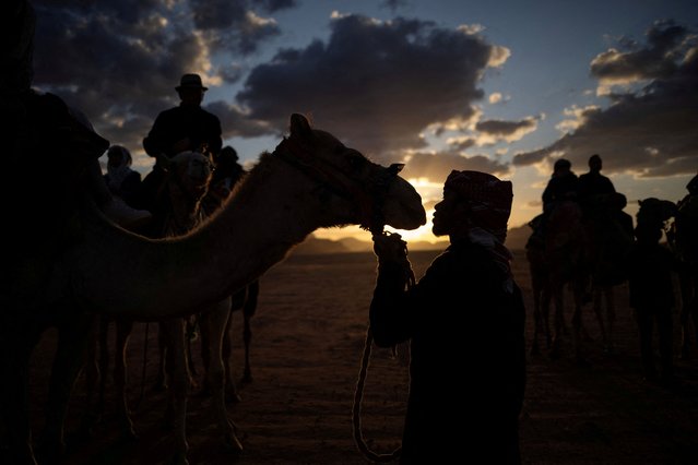 Tourist guide Mohammad Abdelaziz, 28, holds a rope tied to a camel as tourists ride camels in the Wadi Rum desert, Jordan on May 6, 2024. (Photo by Stelios Misinas/Reuters)