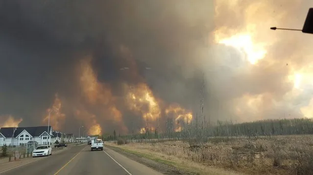 This photo take through a car windshield shows smoke rising from a wildfire rages outside of Fort McMurray, Alberta, Tuesday, May 3, 2016. The entire population of the Canadian oil sands city of Fort McMurray, has been ordered to evacuate as a wildfire whipped by winds engulfed homes and sent ash raining down on residents. (Photo by Mary Anne Sexsmith-Segato/The Canadian Press via AP Photo)