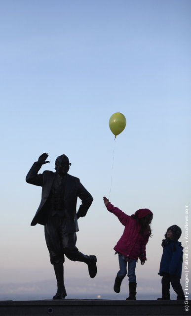 Children with balloons play beside the statue of British comedy legend Eric Morecambe