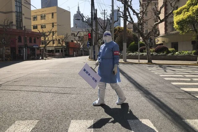 A worker in protective gear holds a sign which reads “Keep one meter apart” along an empty street in a lockdown area in the Jingan district of western Shanghai, Monday, April 4, 2022. (Photo by Chen Si/AP Photo)