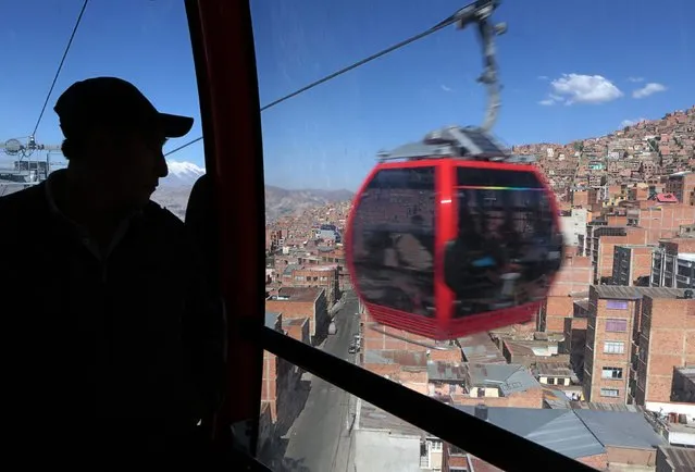 A passenger of a cable car looks out, as another cable car is seen, on the route from La Paz to El Alto, in La Paz, July 23, 2015. (Photo by David Mercado/Reuters)