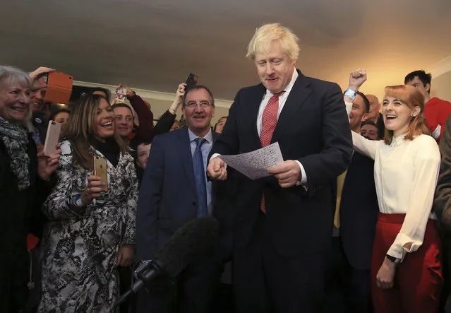 Britain's Prime Minister Boris Johnson reads from his notes as he speaks to supporters and new Sedgefield lawmaker Paul Howell, centre left, during a visit to meet newly elected Conservative party lawmakers at Sedgefield Cricket Club in County Durham, north east England on Saturday December 14, 2019, following his Conservative party's general election victory.  Johnson called on Britons to put years of bitter divisions over the country's EU membership behind them as he vowed to use his resounding election victory to finally deliver Brexit. (Photo by Lindsey Parnaby/Pool via AP Photo)