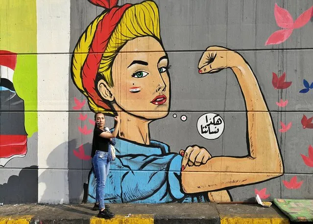 In this Monday, November 18, 2019 photo, a woman poses for a photo in front of graffiti at the Saadoun tunnel, in Baghdad, Iraq. The tunnel that passes under Baghdad’s landmark Tahrir Square has become an ad hoc museum for Iraq's revolution: Young artists draw images and murals that illustrate the country’s tortured past, and the Iraq they aspire to. Arabic reads, “those are our women”. (Photo by Khalid Mohammed/AP Photo)
