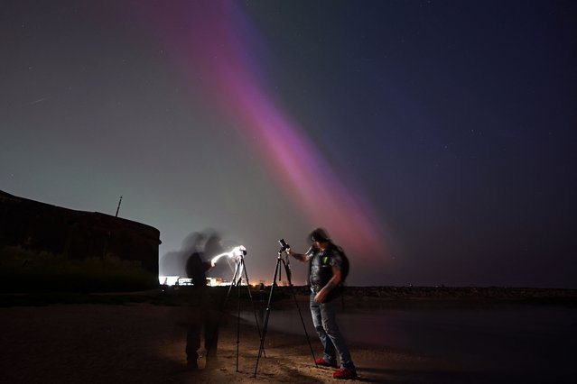 People gather to take pictures of the Aurora Borealis, also known as the Northern Lights, in New Brighton in northwest England late on May 10, 2024. The most powerful solar storm in more than two decades struck Earth, triggering spectacular celestial light shows from Tasmania to Britain – and threatening possible disruptions to satellites and power grids as it persists into the weekend. (Photo by Paul Ellis/AFP Photo)