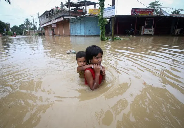 A girl carries her brother as she wades through a flooded road after heavy rains, on the outskirts of Agartala, India, June 18, 2022. (Photo by Jayanta Dey/Reuters)