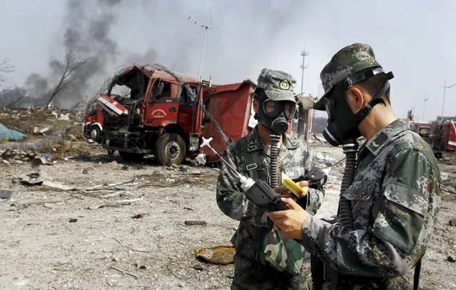 Soldiers of the People's Liberation Army anti-chemical warfare corps work next to a damaged firefighting vehicle at the site of Wednesday night's explosions at Binhai new district in Tianjin, China, August 16, 2015. Chinese soldiers and rescue workers in gas masks and hazard suits searched for toxic materials in China's port of Tianjin on Sunday, days after explosions flattened part of a national development zone. (Photo by Reuters/China Daily)