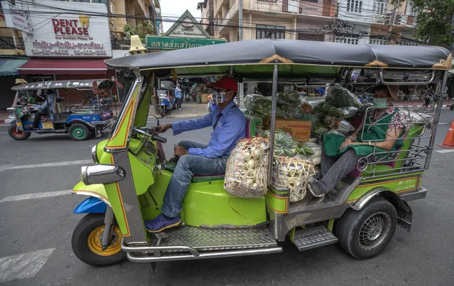 A vendor wearing a face mask is driven by a tuk-tuk, or auto rickshaw, with vegetables for sale at a market in Bangkok, Thailand, Tuesday, April 28, 2020. A month-long state of emergency remains enforced in Thailand to allow its government to impose stricter measures to control the coronavirus that has infected hundreds of people in the Southeast Asian country. (Photo by Sakchai Lalit/AP Photo)