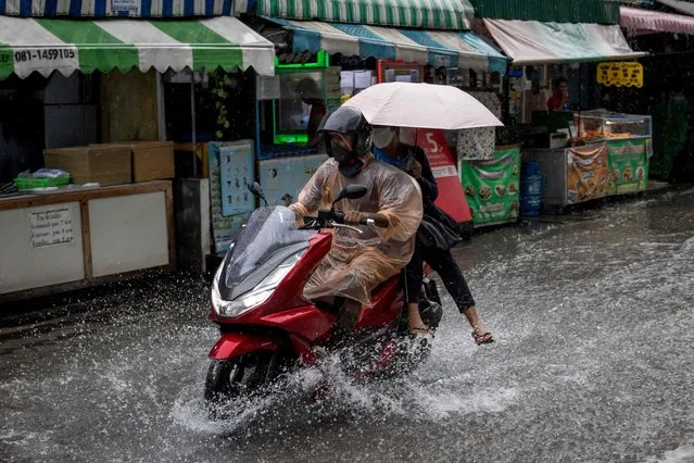 Motorists ride down a flooded street following a heavy downpour of rain in Bangkok on September 13, 2022. (Photo by Jack Taylor/AFP Photo)