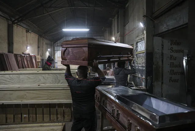 Cesar Ambrosio helps his father carry a coffin at the Bergut Funeral Services factory in Santiago, Chile, Thursday, June 18, 2020. Coffin production has had to increase up to 120%, according to Nicolas Bergerie, owner of the factory. His more basic coffin model is called the COVID model and is made to cope with the increase of deaths during the coronavirus pandemic. (Photo by Esteban Felix/AP Photo)