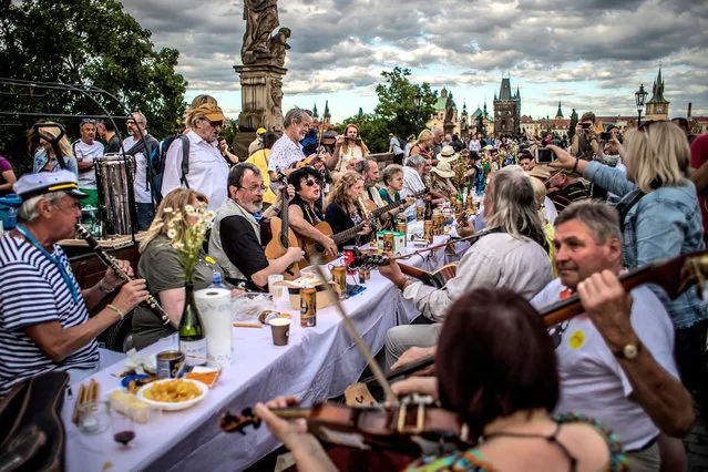 Musicians perform as diners sit at a gigantic table measuring 515 meters (1,690 feet) in length and spanning the entirety of the iconic Charles Bridge in Prague, Czech Republic, 30 June 2020. The massive dinner party came after an easing of the restrictions imposed in a bid to slow down the spread of the pandemic COVID-19 disease caused by the SARS-CoV-2 coronavirus. The event's organizers covered the colossal table with a white tablecloth and adorned it with flowers. Attendees were encouraged to bring their own food and share it with others. The still-low number of foreign visitors to the Czech Republic due to the coronavirus pandemic also provided an opportunity for locals to enjoy one of their city's most famous landmarks without the habitual hubbub from the throngs of tourists that usually crowd the picturesque capital. (Photo by Martin Divíšek/EPA/EFE)