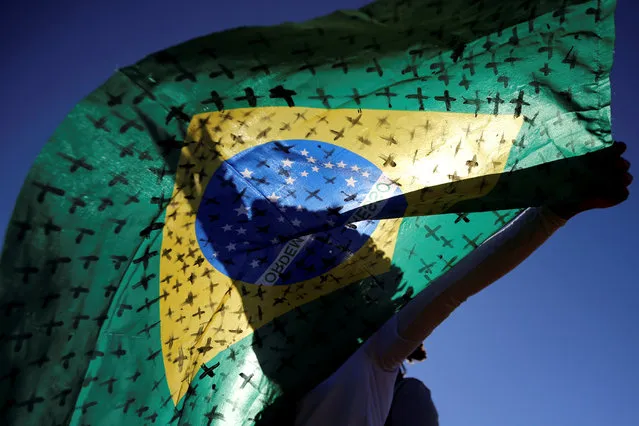 An activist holds a Brazilian flag painted with crosses symbolising the ones who died from the coronavirus disease (COVID-19) in front of the National Congress during a protest against Brazil's President Jair Bolsonaro in Brasilia, Brazil on July 14, 2020. (Photo by Adriano Machado/Reuters)