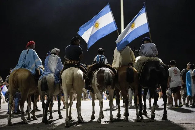 Men dressed in traditional gaucho outfits wait for the pass of the bus taking the Argentine team that worn the World Cup to the training grounds where they will spend the night after landing at Ezeiza airport on the outskirts of Buenos Aires, Argentina, Tuesday, December 20, 2022. (Photo by Rodrigo Abd/AP Photo)