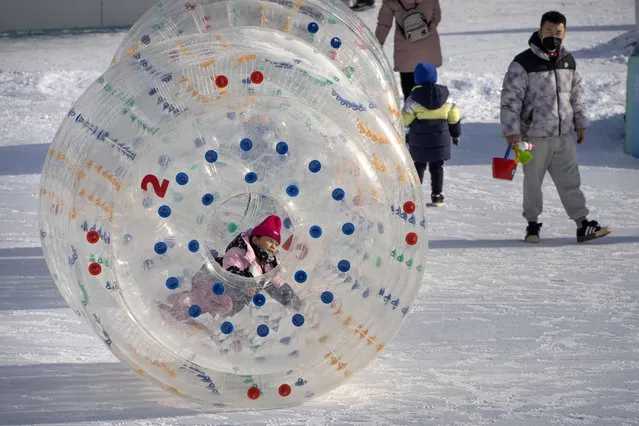 A girl rolls an inflatable tube across the snow at an ice carnival at a public park in Beijing on the first day of the Lunar New Year holiday, Sunday, January 22, 2023. (Photo by Mark Schiefelbein/AP Photo)