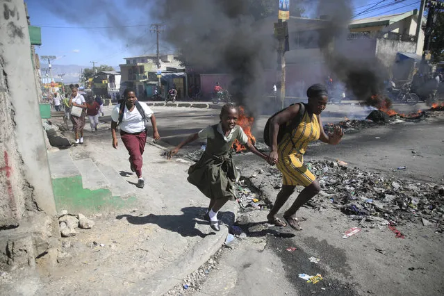 A woman with her daughter walks past a barricade that was set up by members of the police as they protest bad police governance, in Port-au-Prince, Haiti, Thursday, January 26, 2023. (Photo by Joseph Odelyn/AP Photo)