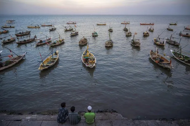 People sit next to traditional boats along the coastline in Surabaya on March 3, 2023. (Photo by Juni Kriswanto/AFP Photo)