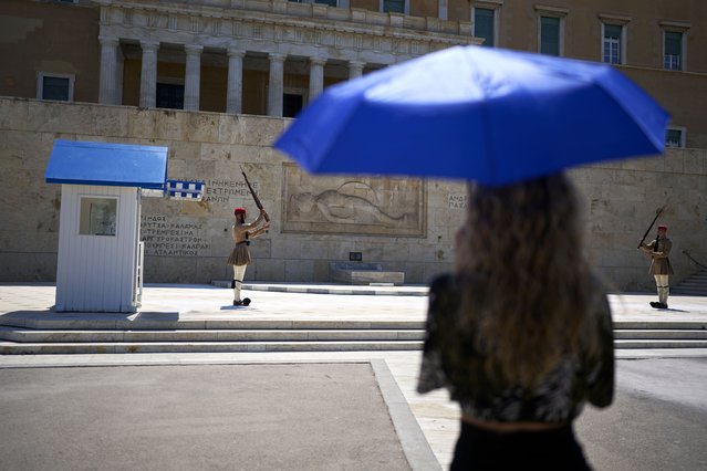 A tourist holds an umbrella to shelter from the sun while watching the changing of the Presidential Guard at the Tomb of the Unknown Soldier, outside the Greek Parliament, during a heatwave in Athens, Thursday, July 17, 2025. (Photo by Petros Giannakouris/AP Photo)