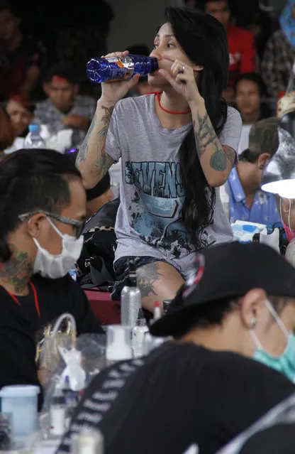 A girl drinks as she gets a tattoo on her leg during Bandung Body Art Festival at in Bandung, West Java, on December 7, 2014. (Photo by Rezza Estily/JG Photo)