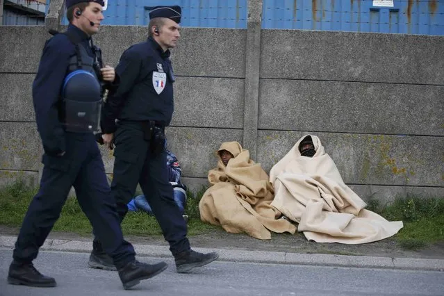 French police patrol near migrants who claim to be minors and are wrapped in blankets to protect themselves from the cold as they prepare to spend the night on a street after the dismantlement of the “Jungle” camp in Calais, France, October 27, 2016. (Photo by Pascal Rossignol/Reuters)