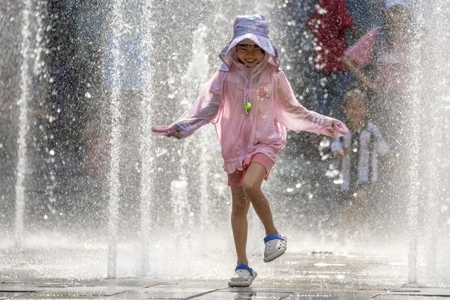 A girl runs as she plays in a fountain at a shopping mall in Beijing, Friday, June 23, 2023. Authorities issued a rare red alert for high temperatures in parts of China's capital on Friday, the highest level of warning, as highs were expected to once again climb to around 40 degrees Celsius (104 degrees Farenheit). (Photo by Mark Schiefelbein/AP Photo)