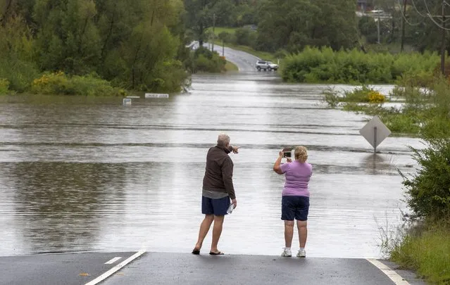 Locals Greg and Kim Spice stand at the edge of a flooded road at Old Pitt Town north west of Sydney, Australia, Sunday, March 21, 2021. Australia's most populous state of New South Wales on Sunday issued more evacuation orders following the worst flooding in decades. (Photo by Mark Baker/AP Photo)