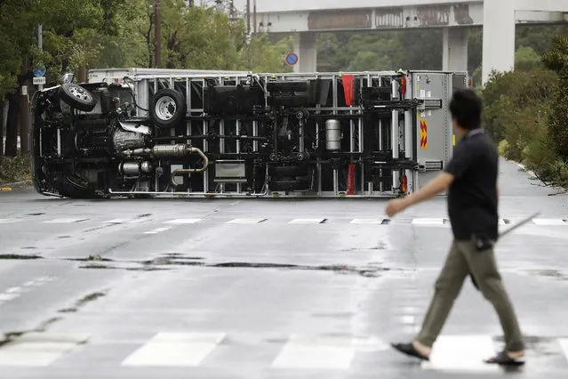 A man looks at a truck overturned following a powerful typhoon in Osaka, western Japan, Tuesday, September 4, 2018. A powerful typhoon blew through western Japan on Tuesday, causing heavy rain to flood the region's main offshore international airport and high winds to blow a tanker into a connecting bridge, disrupting land and air travel. (Photo by Kota Endo/Kyodo News via AP Photo)