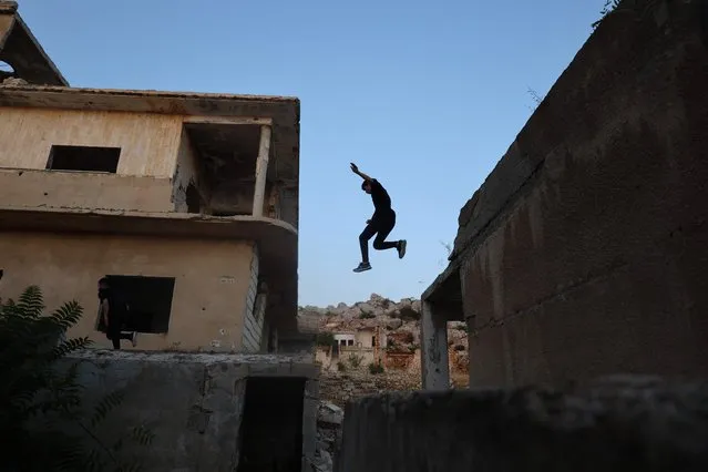 A young Syrian man practises Parkour, an obstacle course method derived from military training, over buildings damaged in fighting between opposition factions and pro-regime forces in the town of Ariha, in Syria's rebel-held northwestern Idlib province, on August 14, 2023. (Photo by Mohammed Al-Rifai/AFP Photo)