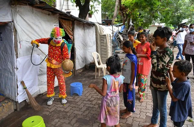 Social worker volunteer Ashok Kurmi, dressed as a clown interacts with children while he sanitises a football and spread awareness to follow the Covid-19 coronavirus safety protocols inside a slum area in Mumbai on June 2, 2021. (Photo by Indranil Mukherjee/AFP Photo)