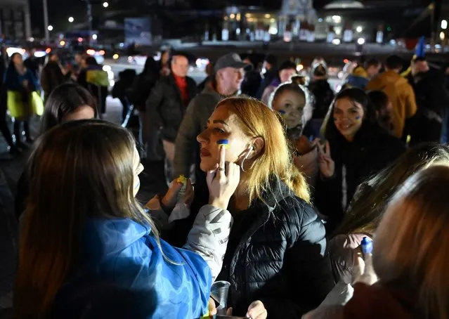 A woman gets colours of Ukranian flag painted on her face as people gather in Maidan square to celebrate the liberation of Kherson, in Kyiv on November 11, 2022, amid the Russian invasion of Ukraine. Ukraine's President Volodymyr Zelensky said on November 11 that Kherson was “ours” after Russia announced the completion of its withdrawal from the regional capital, the only one Moscow captured in nearly nine months of fighting. (Photo by Genya Savilov/AFP Photo)