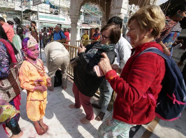Foreign tourists take pictures of a chikd dressed as Hindu God Lord Krishna smeared in colors during the Holi festival celebrations at Durgiana Temple in Amritsar, India, 20 March 2019. Holi is observed at the end of the winter season on the last full moon day of the lunar month Phalguna, which usually falls in the later part of February or March and is celebrated by people throwing colored powder and colored water at each other. (Photo by Raminder Pal Singh/EPA/EFE)