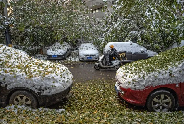 A delivery driver rides a scooter passed cars covered in snow and leaves following a snowfall on November 7, 2021 in Beijing, China. Beijing, which averages less than seven days of snow annually, is set to host the Beijing 2022 Winter Olympics next February. (Photo by Kevin Frayer/Getty Images)