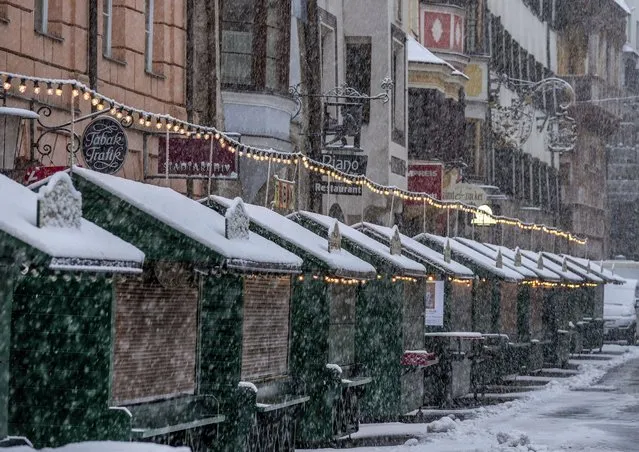 Christmas booths are all closed on the Christmas market in Innsbruck, Austria, as snow falls on Sunday, November 28, 2021. Austria is in a lockdown following a spike in COVID-19 infections. (Photo by Michael Probst/AP Photo)