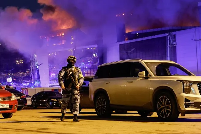 A Russian law enforcement officer walks at a parking area near the burning Crocus City Hall concert venue following a shooting incident, outside Moscow, Russia, on March 22, 2024. (Photo by Maxim Shemetov/Reuters)